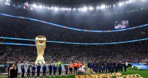 Jugadores de una selección nacional reunidos en el círculo central durante la interpretación de los himnos en el Mundial